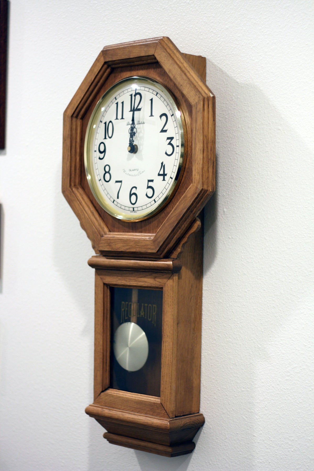 A wooden pendulum clock hangs on a white wall.