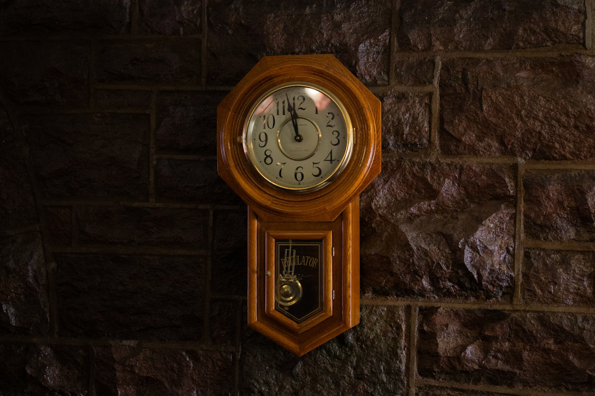 A wooden grandfather clock hangs on a stone wall.
