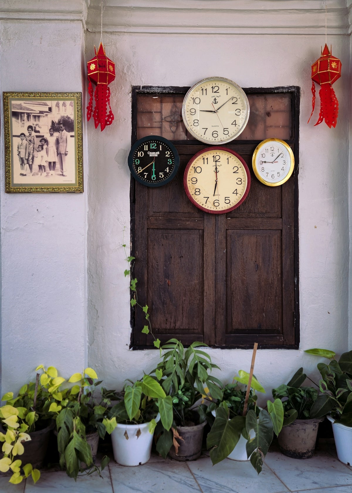 Four clocks hang above a wooden window with plants.