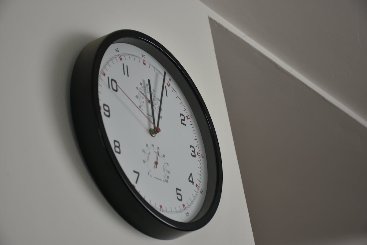 A round clock with black frame on a white wall.