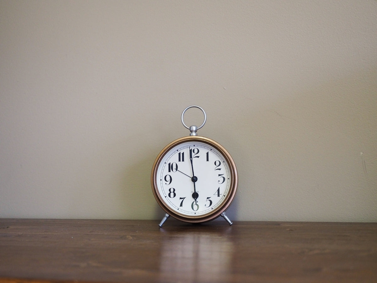 A vintage alarm clock sits on a wooden surface.