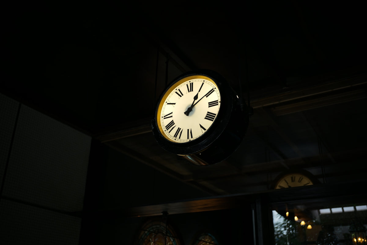 A vintage clock with roman numerals hangs indoors.